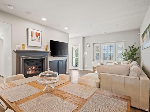 living area with a glass covered fireplace, wood finished floors, recessed lighting, and baseboards