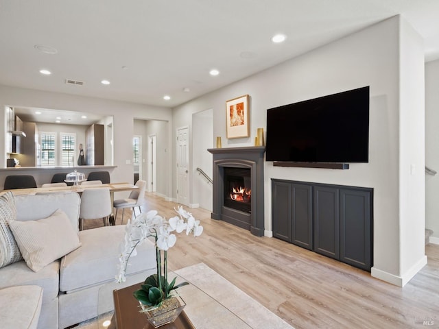 living area with visible vents, recessed lighting, light wood finished floors, and a lit fireplace