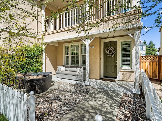 property entrance featuring an outdoor hangout area, fence, stucco siding, and a balcony