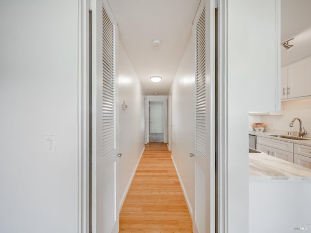 corridor featuring a sink, baseboards, and light wood-type flooring