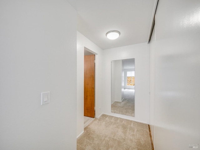 hallway featuring light colored carpet and baseboards