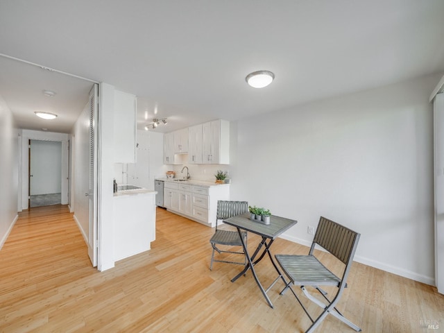 kitchen with baseboards, light countertops, white cabinetry, light wood finished floors, and a sink