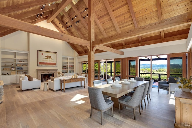 dining area with wooden ceiling, a high end fireplace, beamed ceiling, light wood-style flooring, and high vaulted ceiling