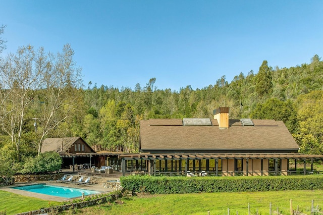 back of house with a wooded view, a chimney, a yard, and an outdoor pool
