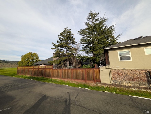 view of property exterior with fence, stone siding, and stucco siding
