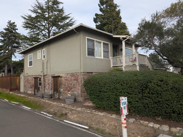 view of side of property with stucco siding, stone siding, and fence