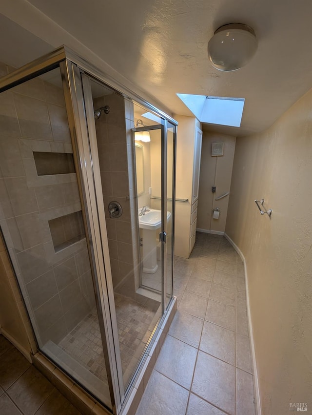 full bath featuring a shower stall, a skylight, a sink, and tile patterned flooring