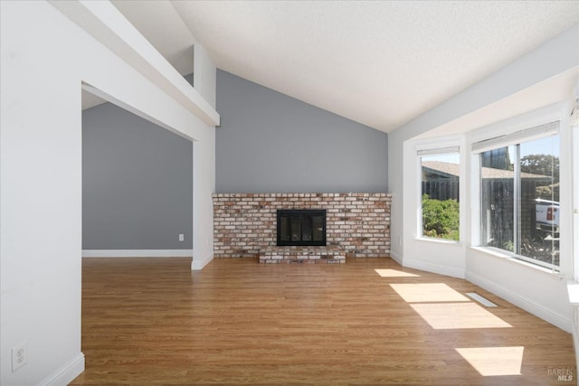 unfurnished living room with wood finished floors, a fireplace, baseboards, lofted ceiling, and visible vents