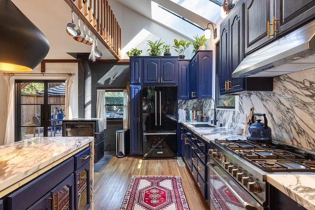 kitchen featuring a sink, under cabinet range hood, light wood-style flooring, stainless steel gas range oven, and freestanding refrigerator