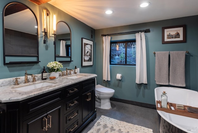 bathroom with double vanity, toilet, a freestanding bath, and a sink