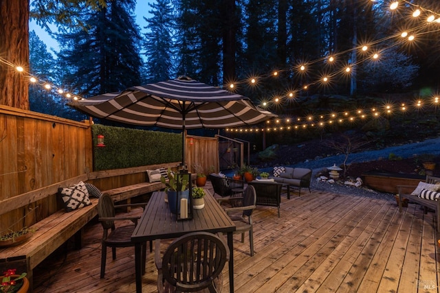 deck at night featuring fence and an outdoor hangout area
