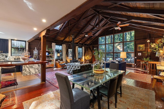 dining room with beamed ceiling, wood-type flooring, wooden walls, a ceiling fan, and high vaulted ceiling