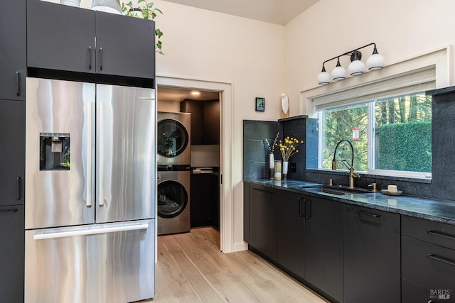 kitchen featuring light wood-style flooring, dark cabinets, a sink, stacked washer and clothes dryer, and freestanding refrigerator