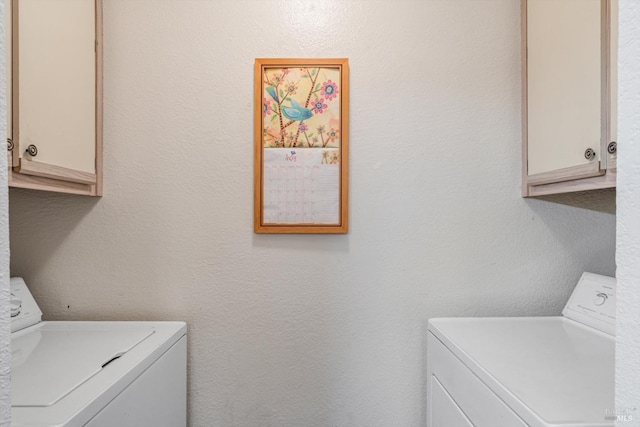 laundry room featuring cabinet space, a textured wall, and washer and clothes dryer