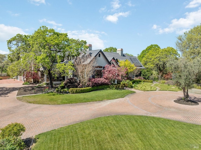 view of front of property with a front lawn, a chimney, curved driveway, and roof mounted solar panels