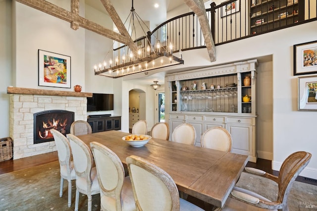 dining space with arched walkways, wood finished floors, a fireplace, and a towering ceiling