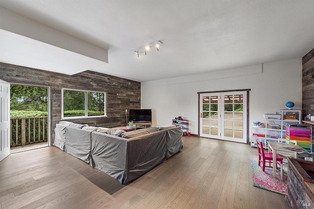 living room featuring a textured ceiling, french doors, wooden walls, and hardwood / wood-style flooring