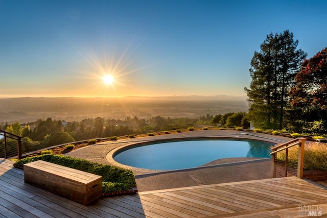 pool at dusk with an outdoor pool and a deck