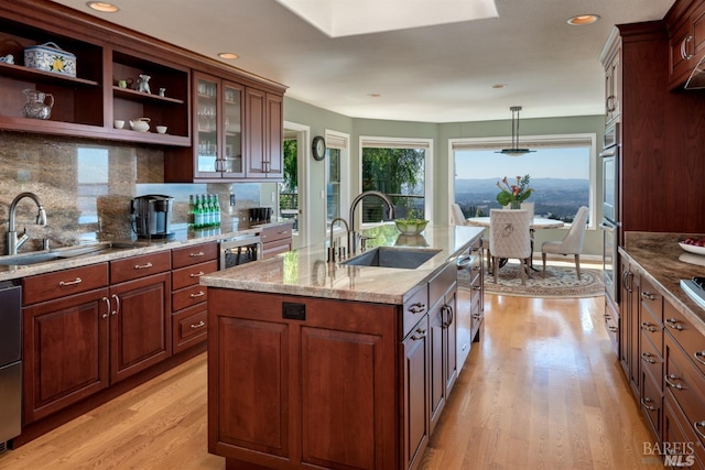 kitchen with light stone countertops, light wood-style floors, a sink, and a center island with sink