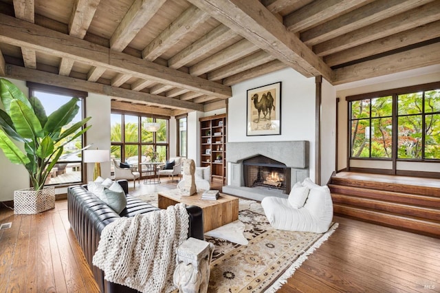 living area with built in features, visible vents, a warm lit fireplace, hardwood / wood-style flooring, and beam ceiling