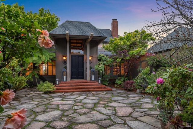 exterior entry at dusk with roof with shingles and a chimney