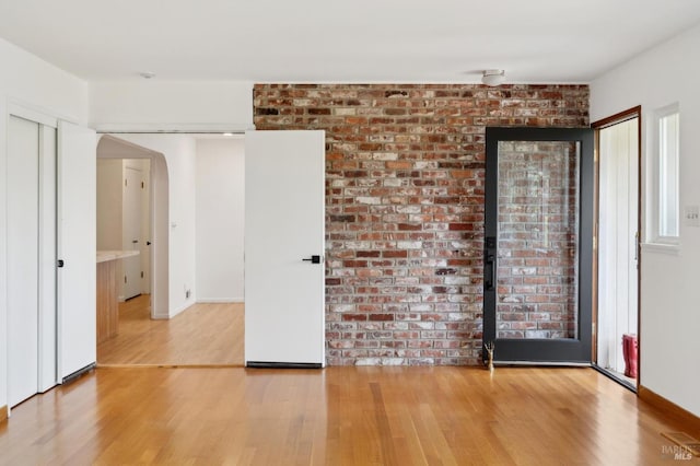 spare room featuring arched walkways, wood finished floors, and baseboards