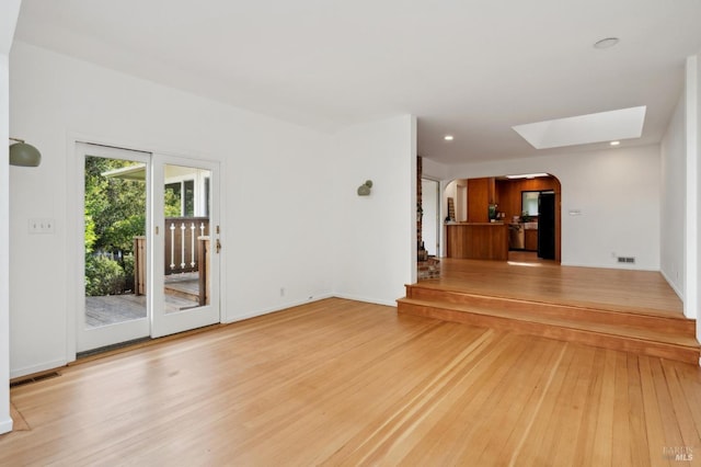 unfurnished living room with recessed lighting, arched walkways, light wood-style flooring, and a skylight