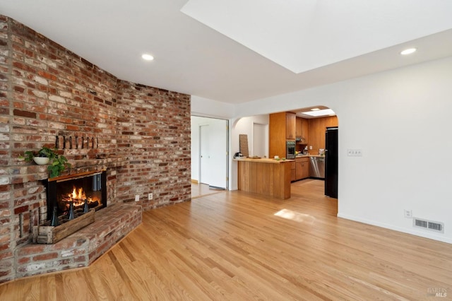 unfurnished living room featuring recessed lighting, a brick fireplace, visible vents, arched walkways, and light wood finished floors