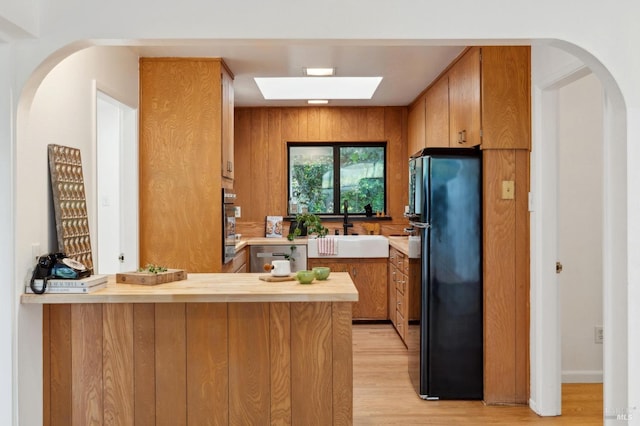 kitchen with freestanding refrigerator, a peninsula, light wood-type flooring, light countertops, and a sink
