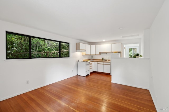 kitchen with white cabinets, light countertops, wood finished floors, white range with gas stovetop, and baseboards