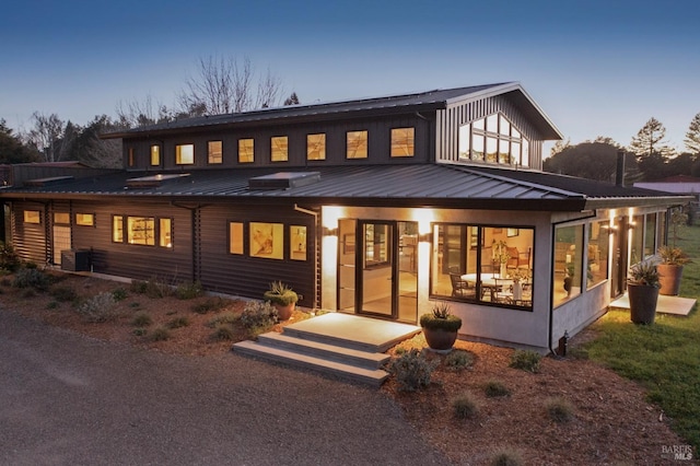 back of house with central AC unit, a sunroom, metal roof, and a standing seam roof