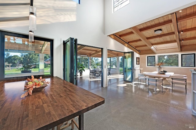 dining area with wooden ceiling, beamed ceiling, a high ceiling, and plenty of natural light