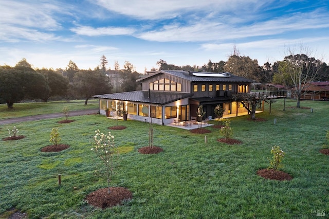 rear view of property with a yard, a patio, metal roof, and roof mounted solar panels