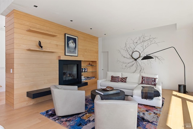 living room featuring wood finished floors, wooden walls, and a glass covered fireplace