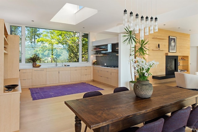 dining space with a skylight, light wood finished floors, and a fireplace with raised hearth