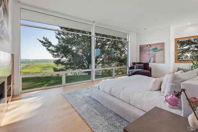 bedroom with expansive windows, a fireplace, and wood finished floors