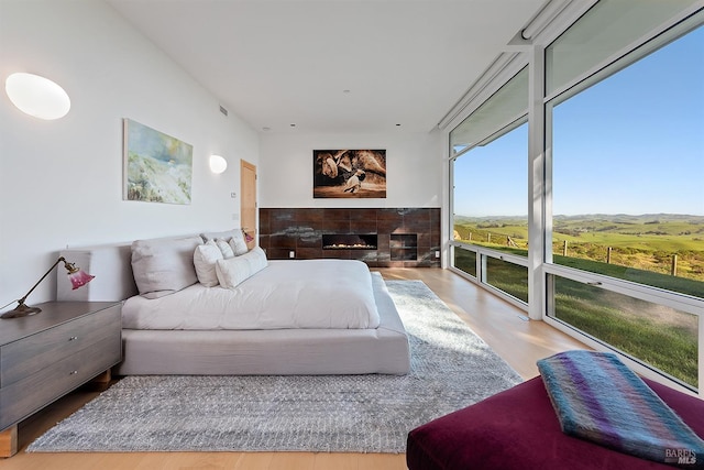bedroom featuring visible vents, floor to ceiling windows, a fireplace, wood finished floors, and access to outside