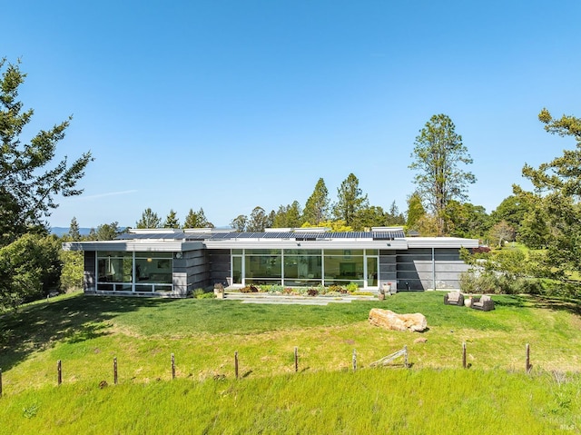 back of house with solar panels, a sunroom, and a lawn