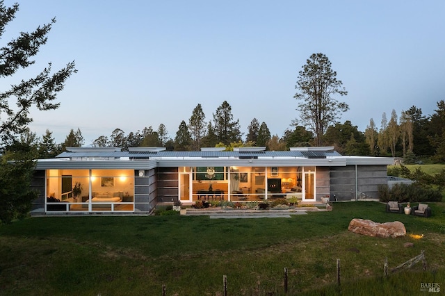 back of property with a yard, a sunroom, and roof mounted solar panels