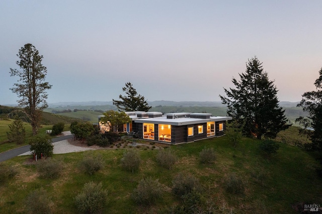 back of property at dusk with a mountain view and a lawn
