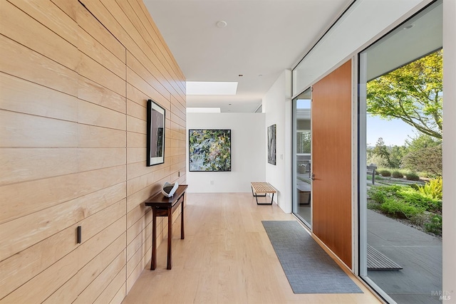 hallway with wood walls, light wood-style flooring, and a skylight