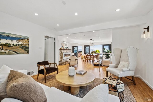 living room featuring visible vents, baseboards, a stone fireplace, recessed lighting, and light wood-type flooring