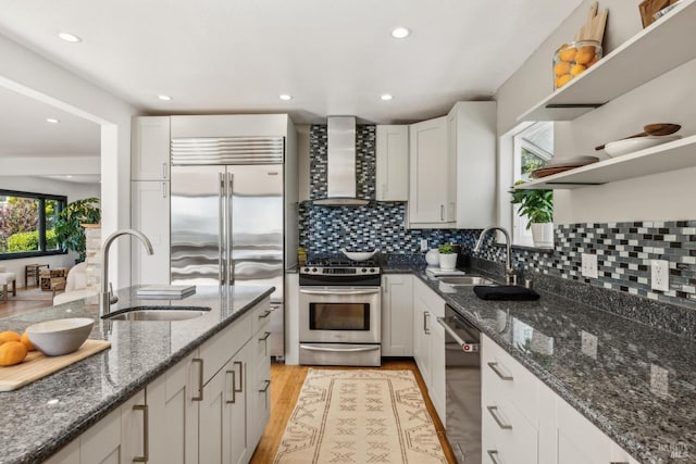kitchen featuring wall chimney range hood, open shelves, stainless steel appliances, and a sink
