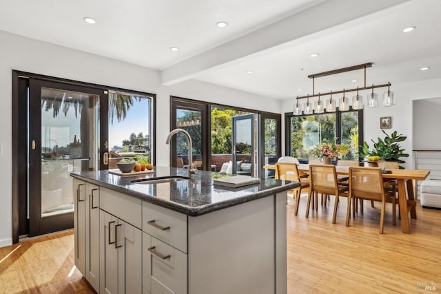 kitchen with beam ceiling, light wood-type flooring, recessed lighting, a sink, and dark stone countertops