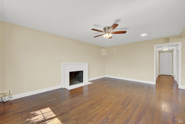 unfurnished living room with dark wood-type flooring, baseboards, ceiling fan, and a fireplace with flush hearth