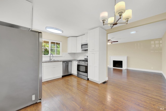 kitchen with backsplash, white cabinets, stainless steel appliances, ceiling fan with notable chandelier, and wood finished floors