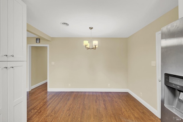 unfurnished dining area with visible vents, baseboards, an inviting chandelier, and wood finished floors