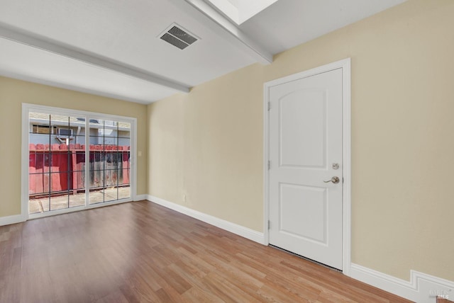 spare room featuring visible vents, baseboards, wood finished floors, and beamed ceiling