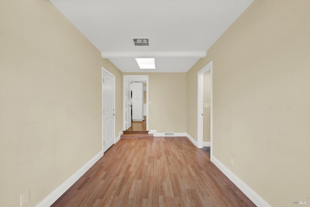 hall featuring light wood-style flooring, baseboards, and visible vents