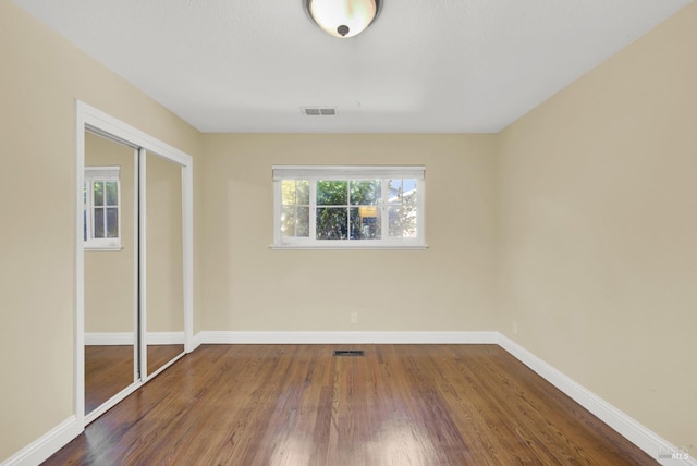 unfurnished bedroom featuring wood finished floors, visible vents, a closet, and baseboards